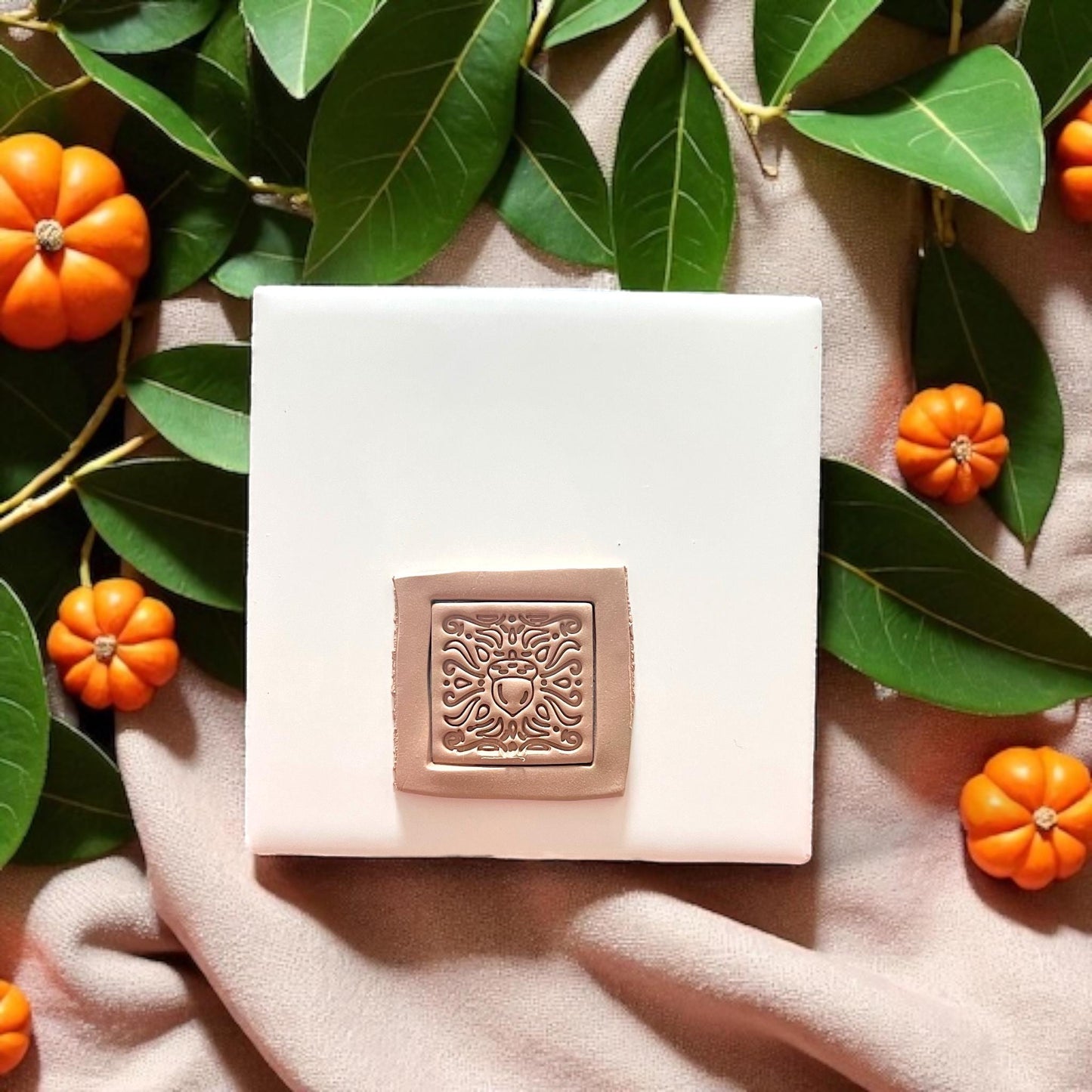 Square acorn motif clay imprint surrounded by pumpkins and greenery