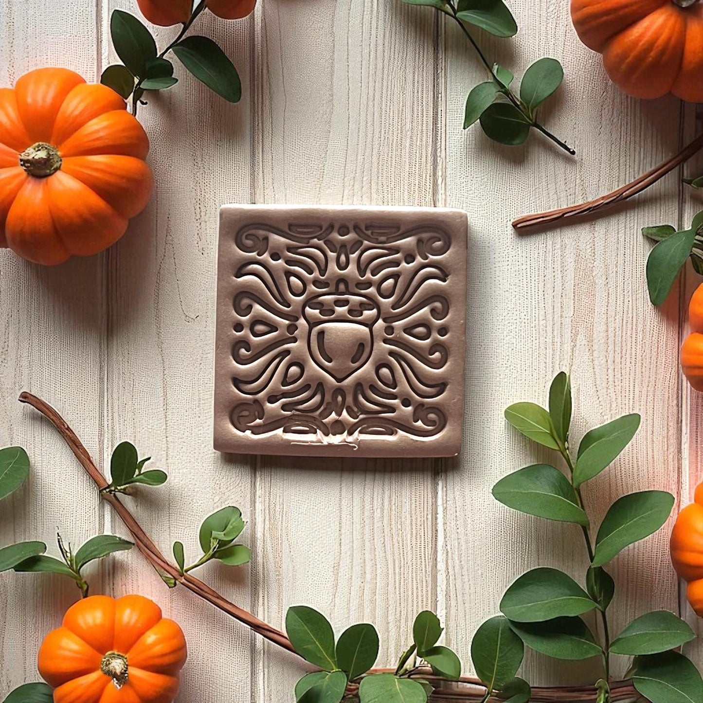Clay tile with acorn foliage design on soft draped fabric and leaves