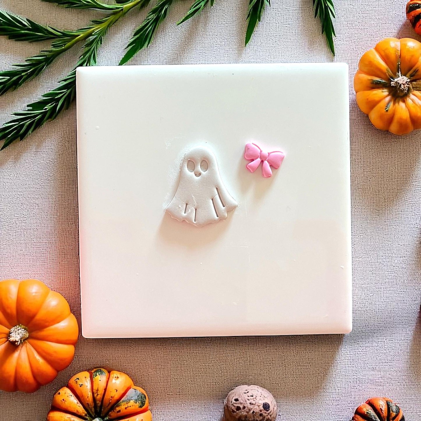 Halloween ghost and bow clay shapes on display with pumpkins and greenery