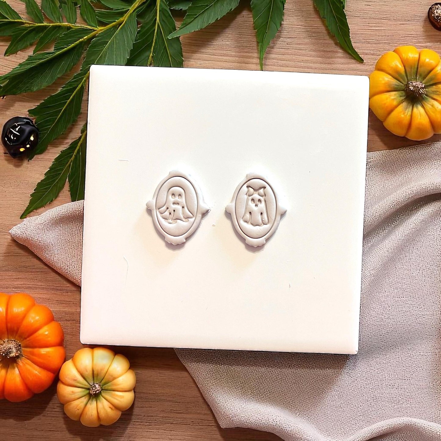 Ghost couple clay impressions in ornate frames surrounded by mini pumpkins and leaves