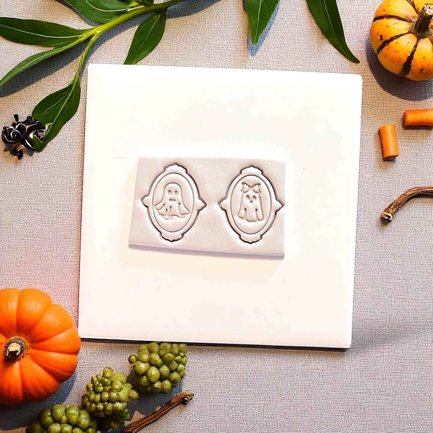 Mr. and Mrs. ghost cutters pressed in clay on white tile with pumpkins and greenery