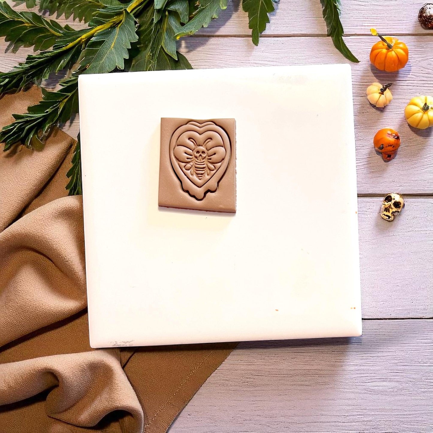 Clay imprint of gothic moth leaf cutter on white tile with mini pumpkins and foliage