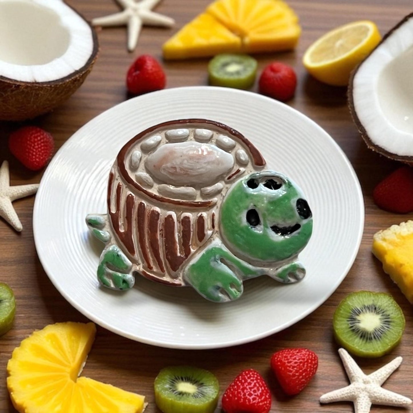Glazed ceramic version of coconut turtle cutter styled on plate with fruit