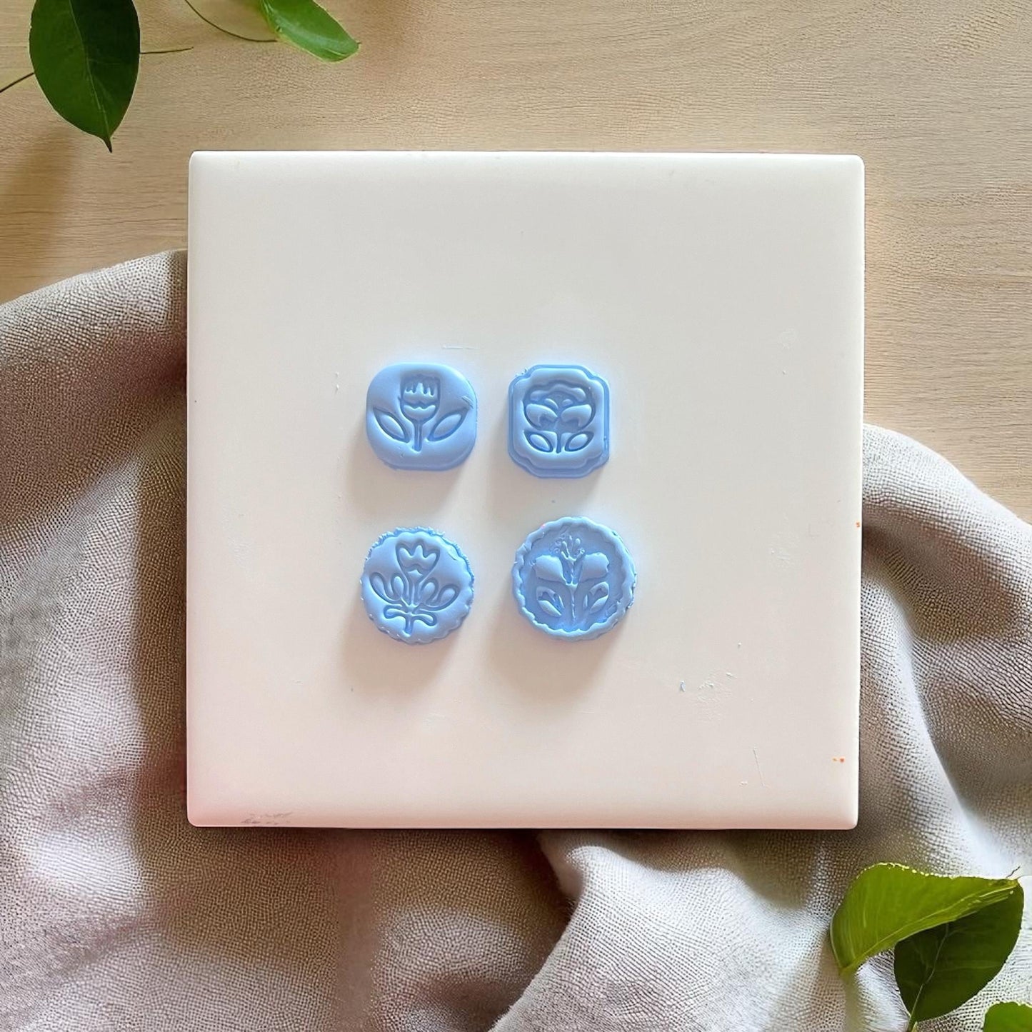four flower charm shapes cut out of blue clay