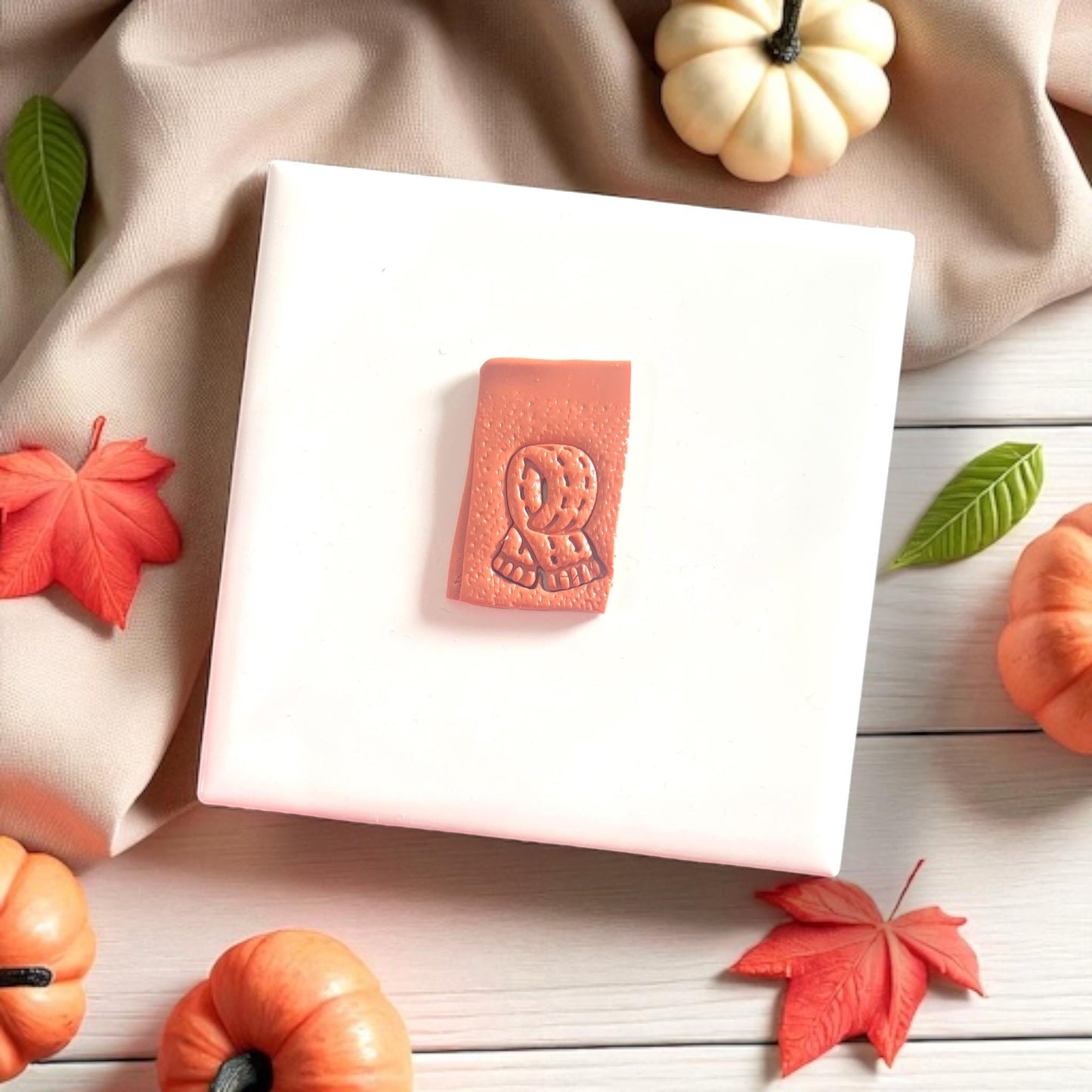 Fall scarf imprint on clay slab styled with pumpkins and autumn leaves