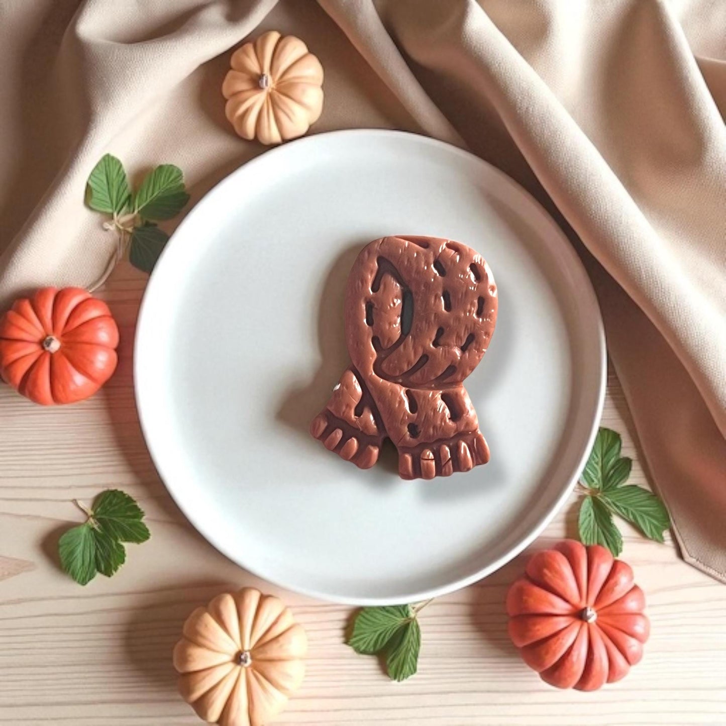Close-up of large clay scarf cutout on plate styled with pumpkins and fall decor