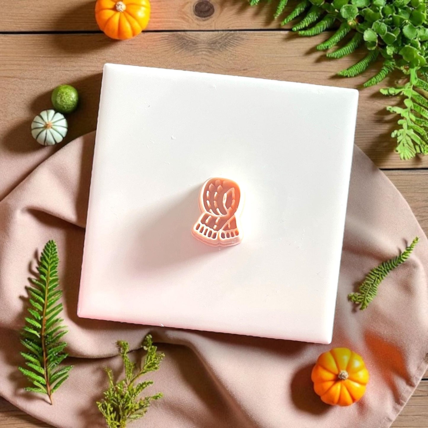 Clay cutter shaped like cozy scarf styled with pumpkins and greenery