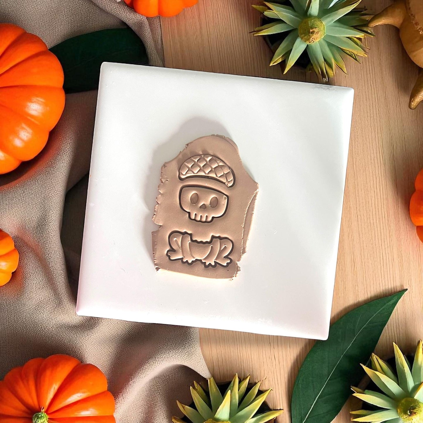 Skull frog clay impression with acorn hat on white tile and pumpkins