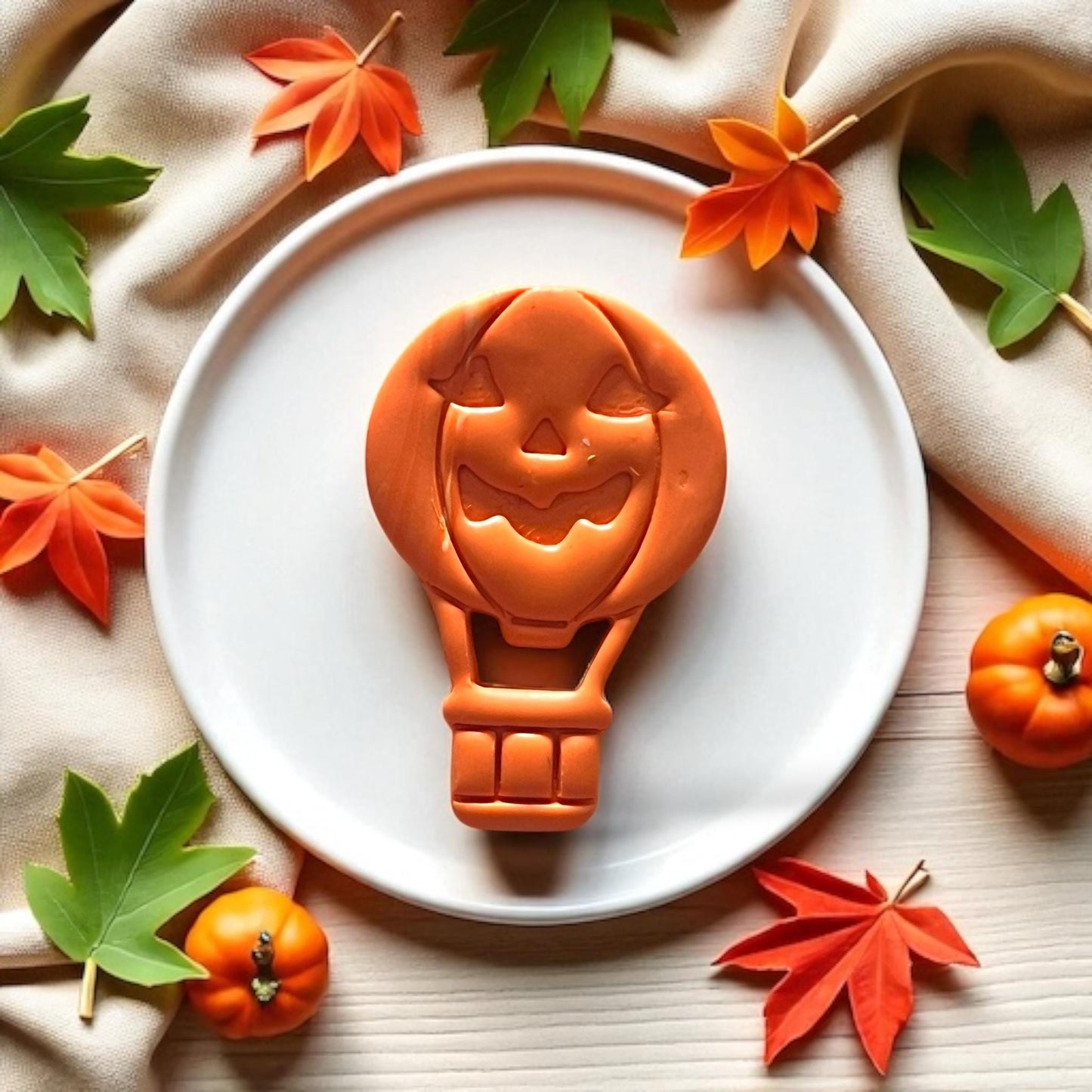 Finished orange jack o lantern balloon clay piece on white plate with leaves