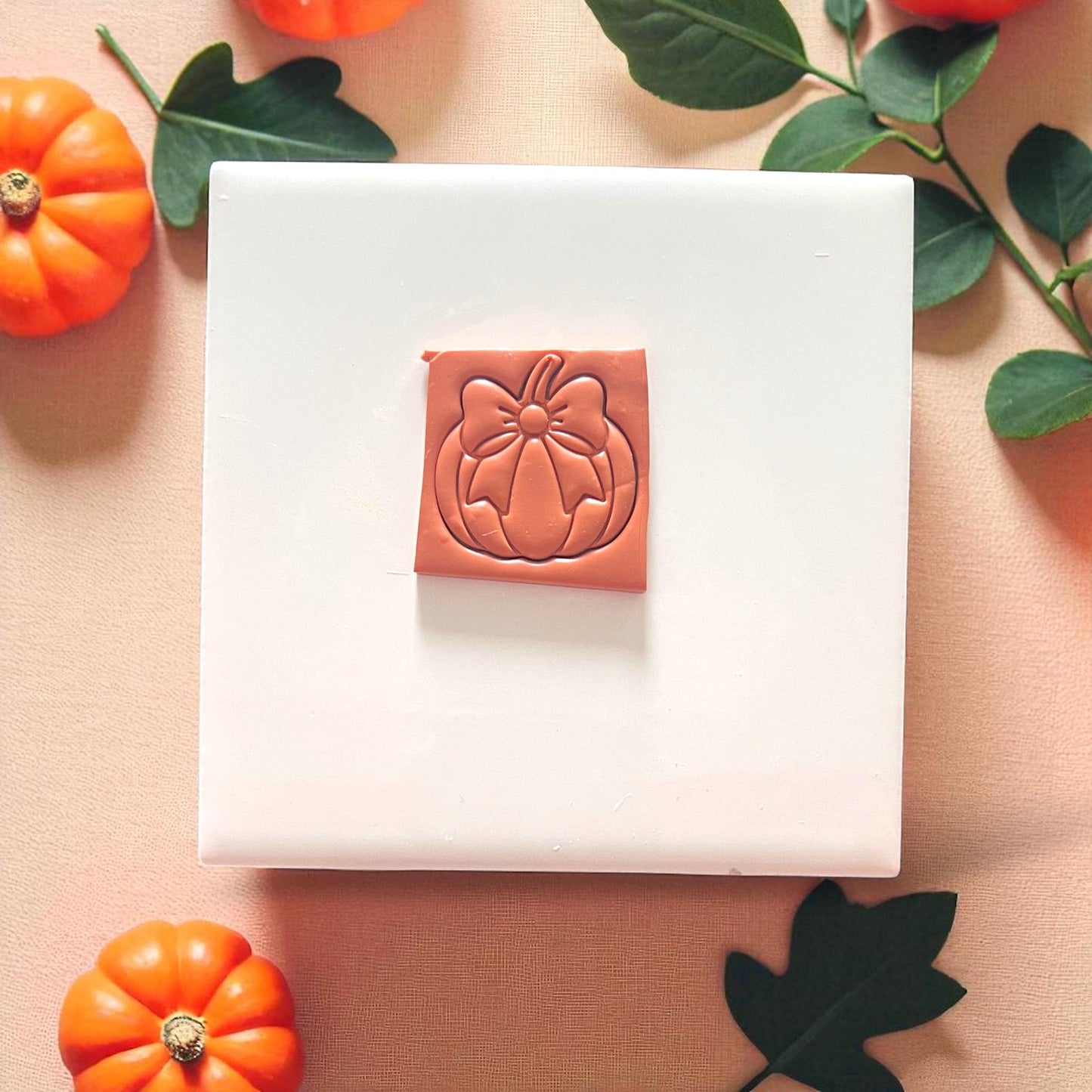 Pumpkin with bow clay earring on white tile