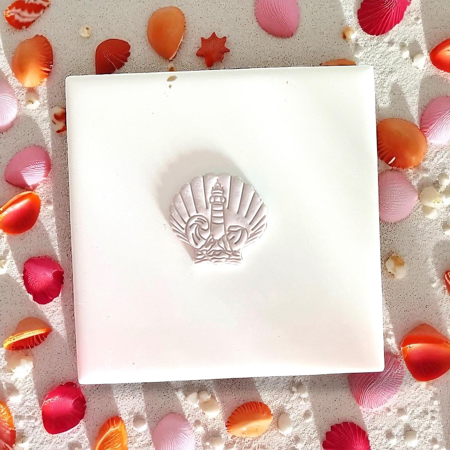 Shell-shaped clay slab with lighthouse and wave motif, styled with coral petals
