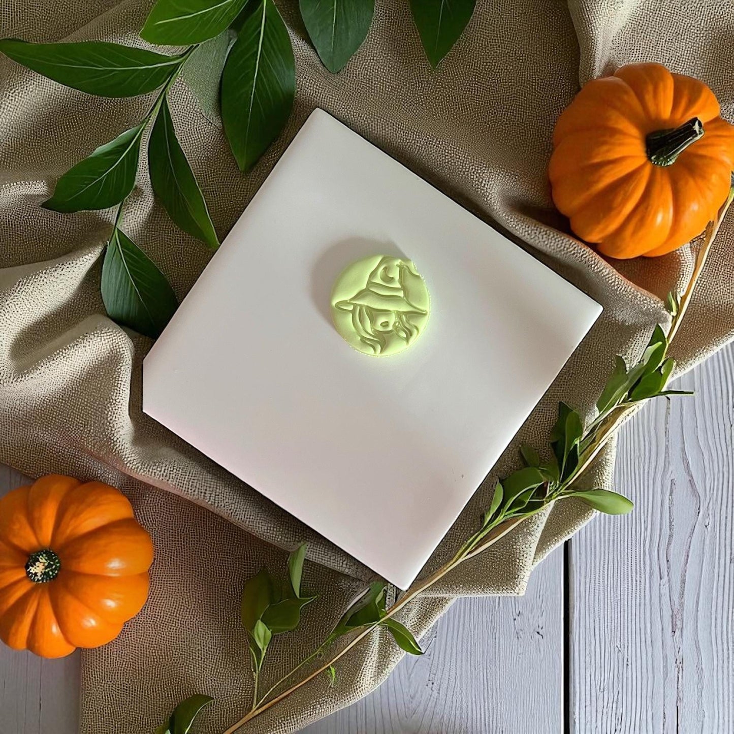 Sexy witch polymer clay imprint centered on white tile with pumpkins and greenery