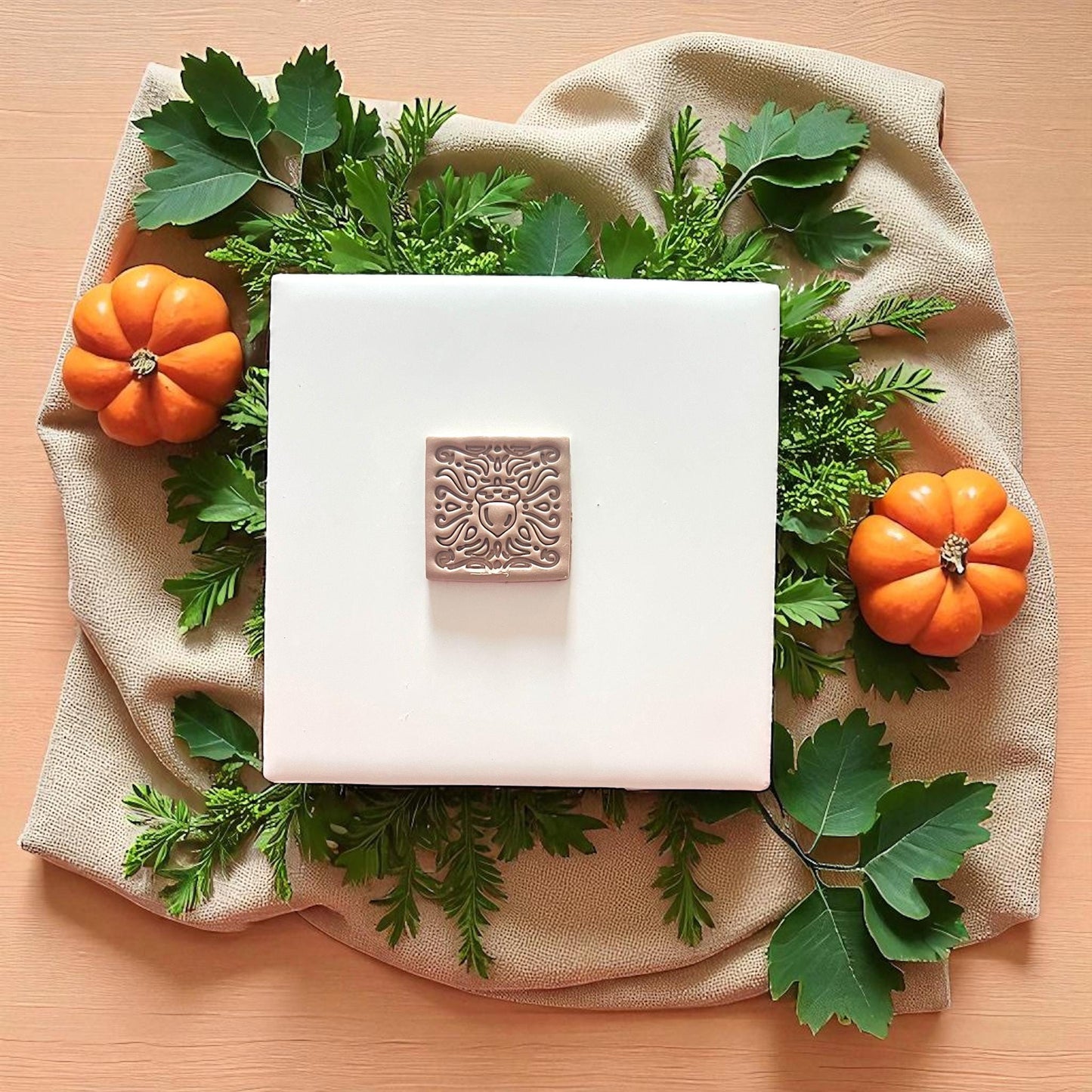 Square clay tile featuring acorn design on a neutral green backdrop