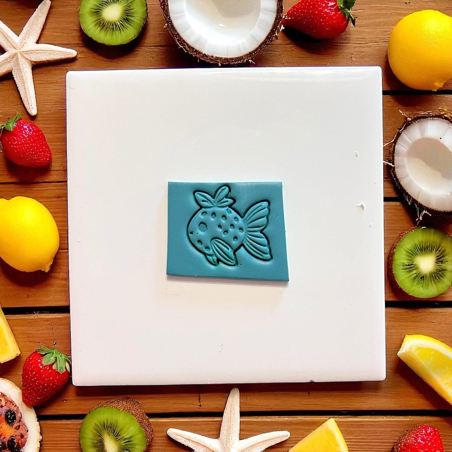 Strawberry fish impression in teal clay surrounded by tropical fruits