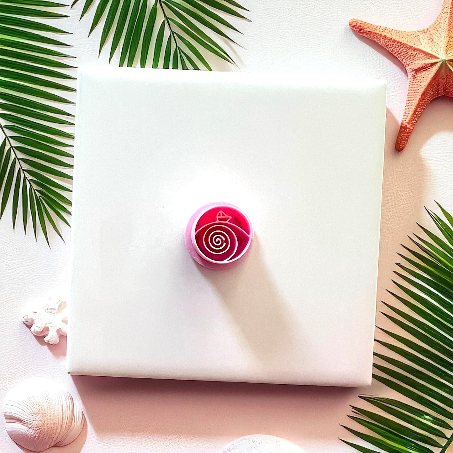 Pink cutter with paper boat and spiral waves design on white tile with palm leaves and starfish.
