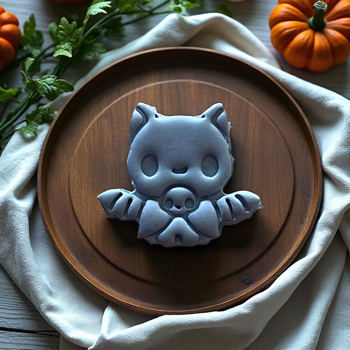 Large gray baby bat clay piece displayed on wooden plate with pumpkins and fabric.