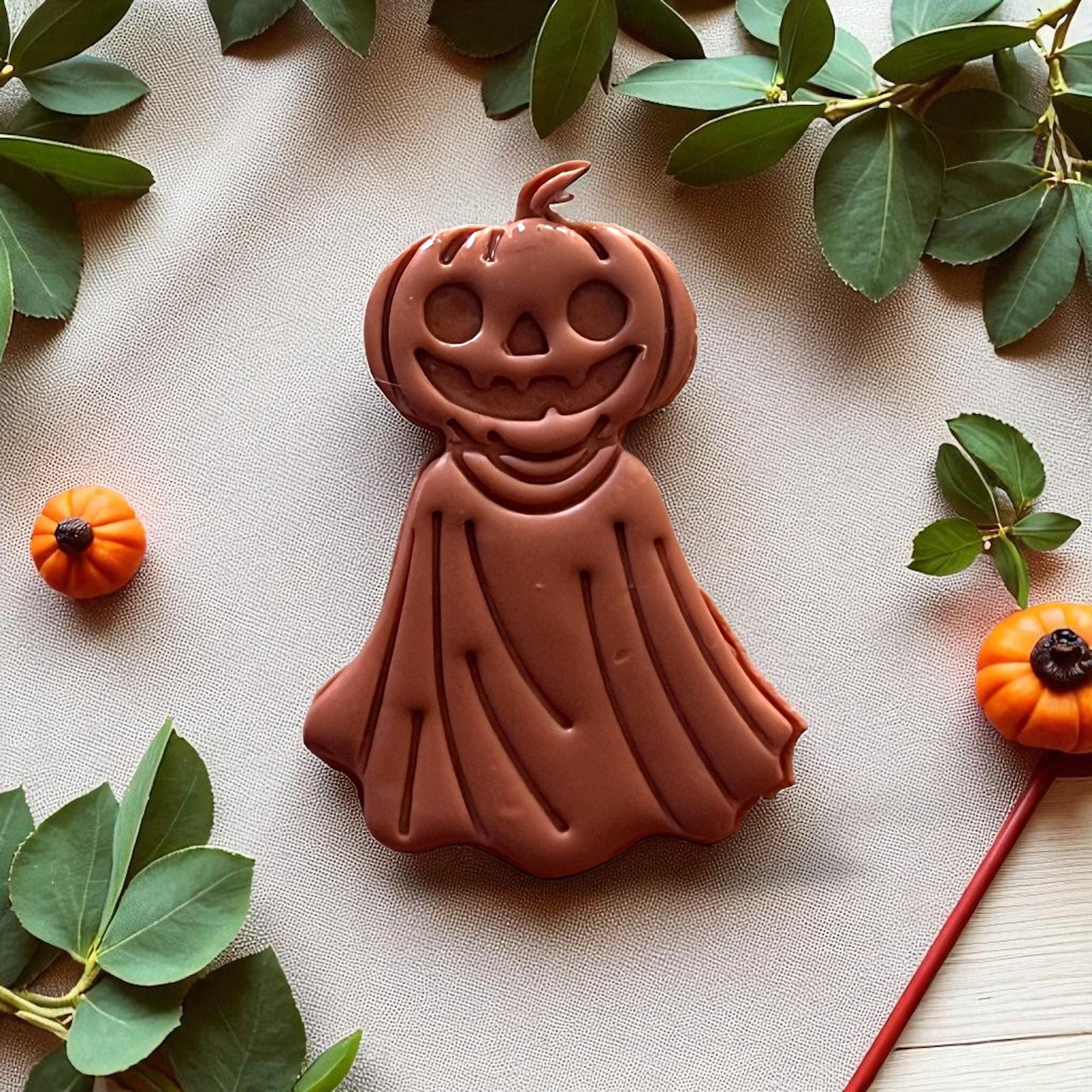 Large orange pumpkin ghost clay piece on fabric with pumpkins and greenery.