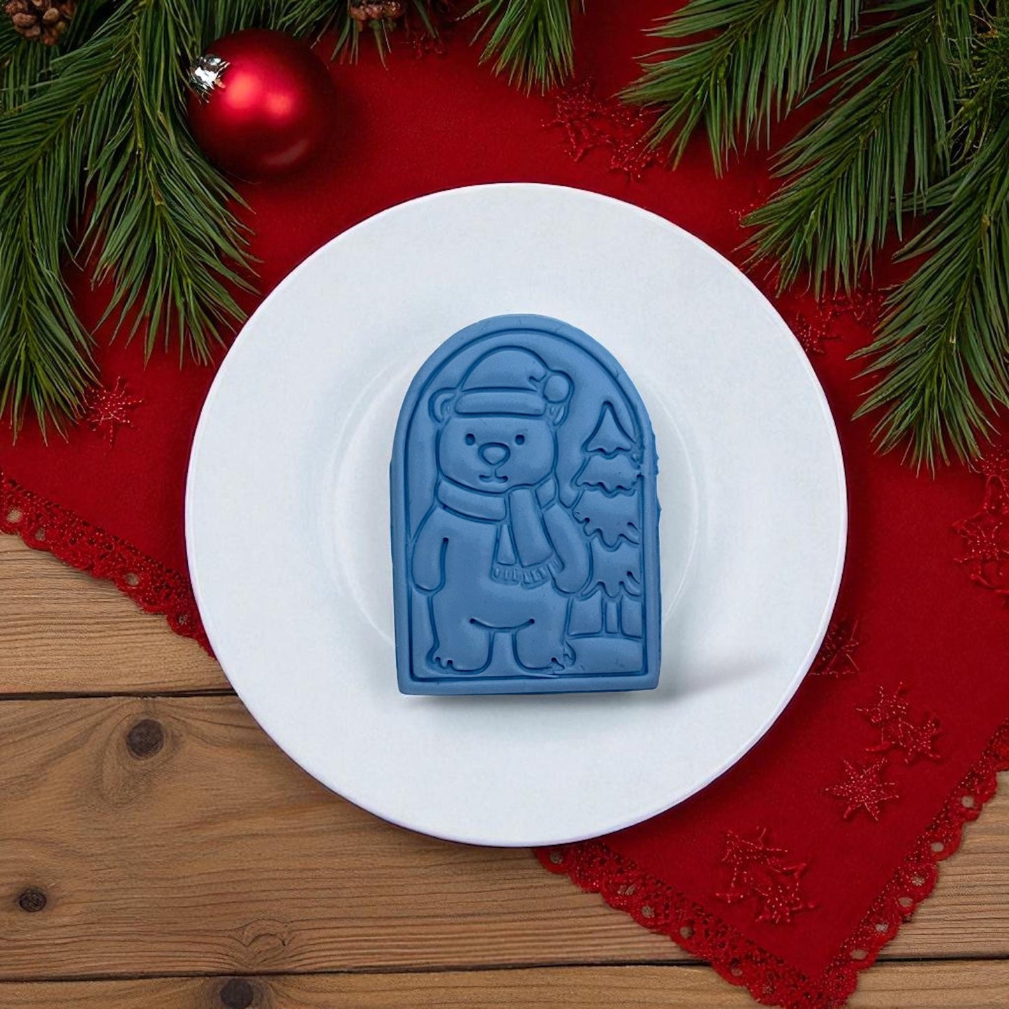 Blue polar bear clay imprint and pink cutter side by side on white tile with Christmas greenery.