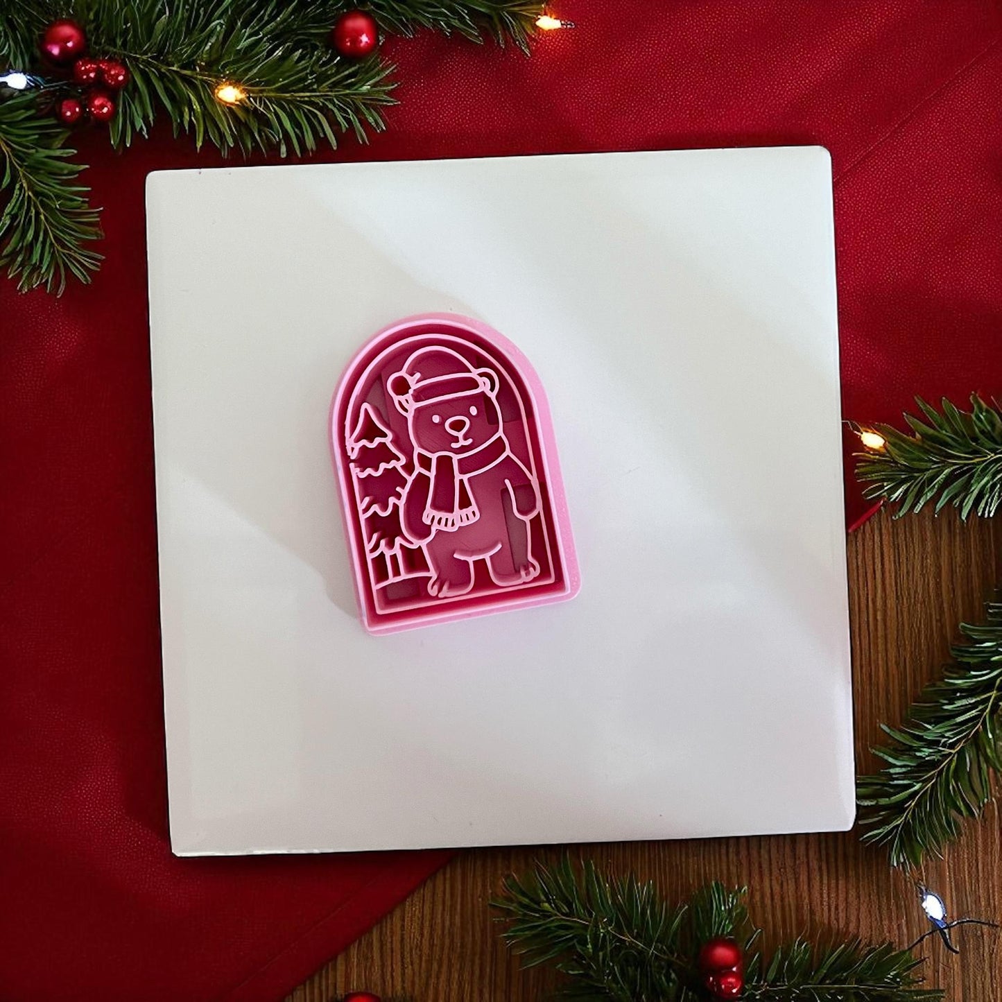 Pink Christmas polar bear clay cutter on white tile with red background and pine branches.