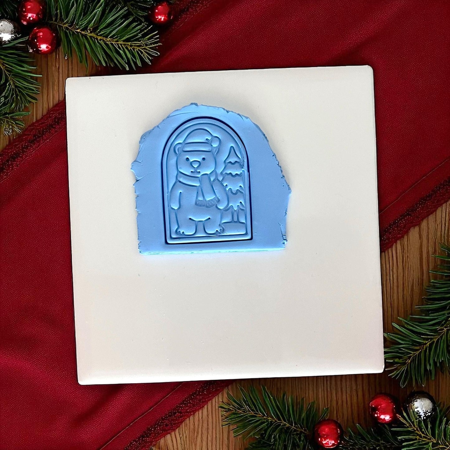 Blue polar bear clay imprint pressed into clay on white tile with red cloth and ornaments.