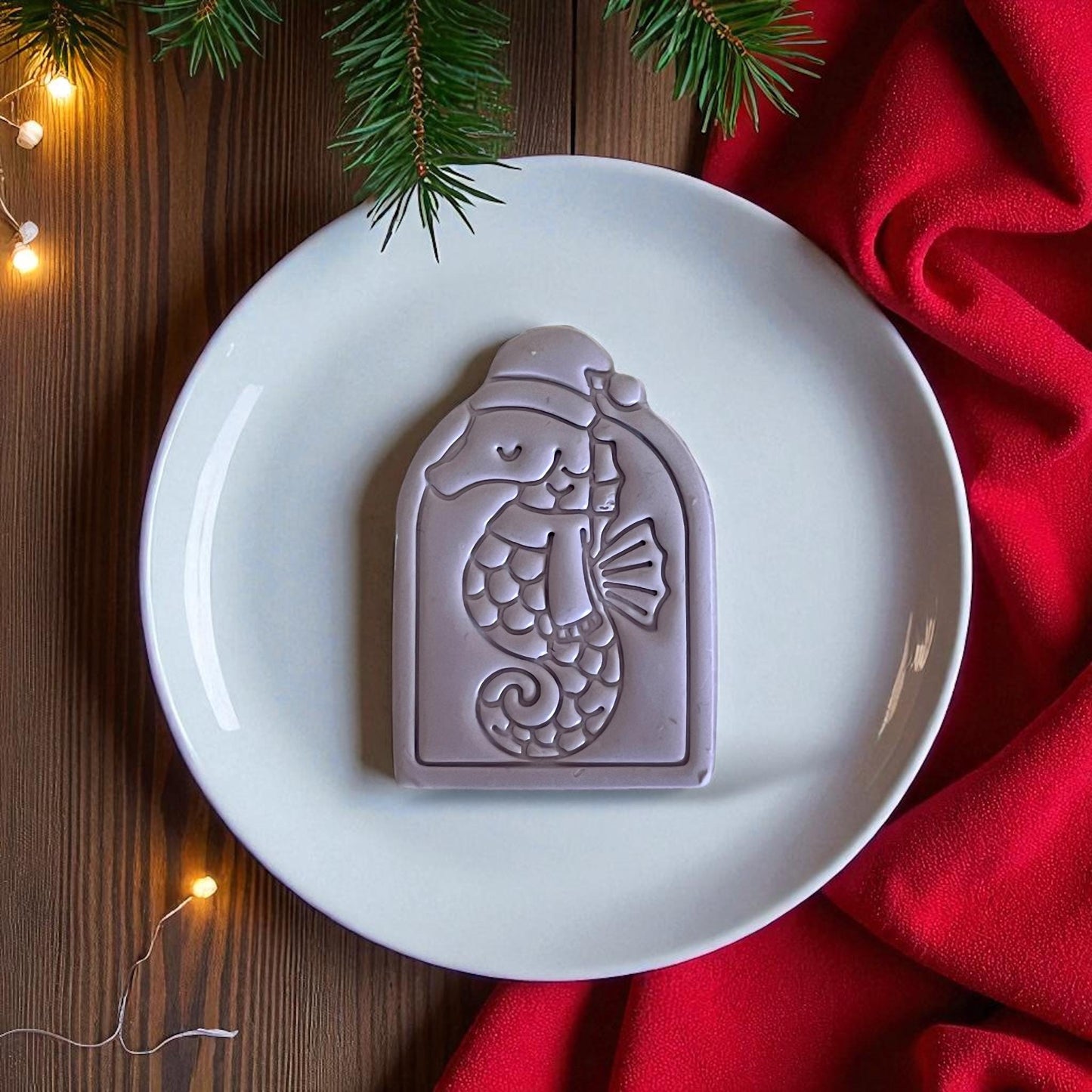 Purple seahorse clay imprint displayed on white plate with red fabric and pine greenery.