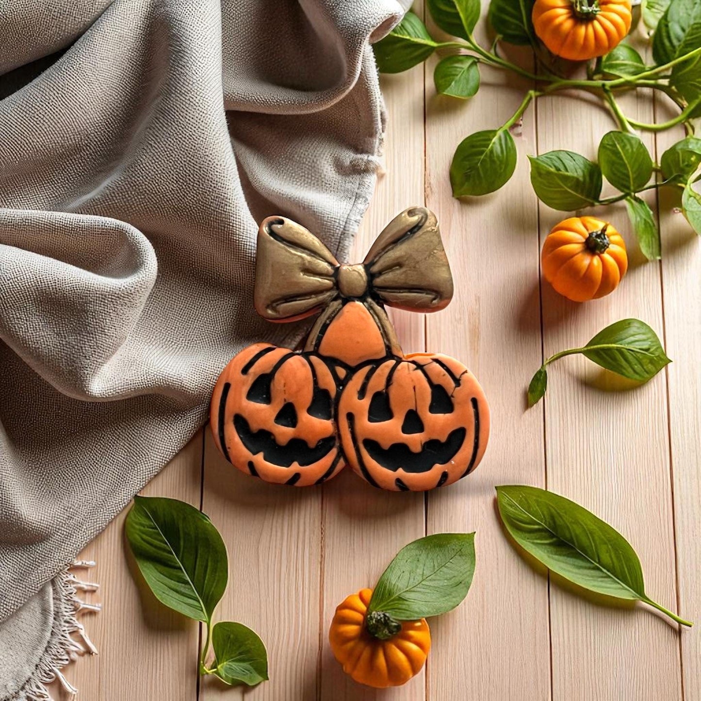Pumpkin cherry bow clay imprint in orange and gold on wooden background with pumpkins and greenery.