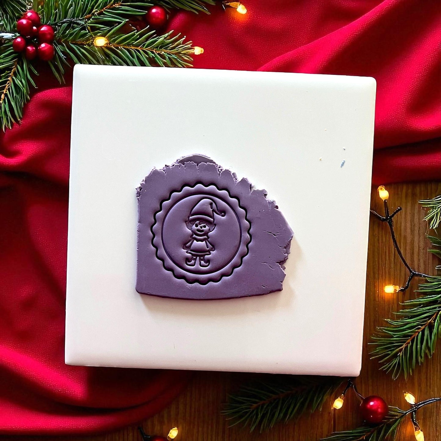 Purple elf clay imprint on clay slab with red fabric and holiday lights.