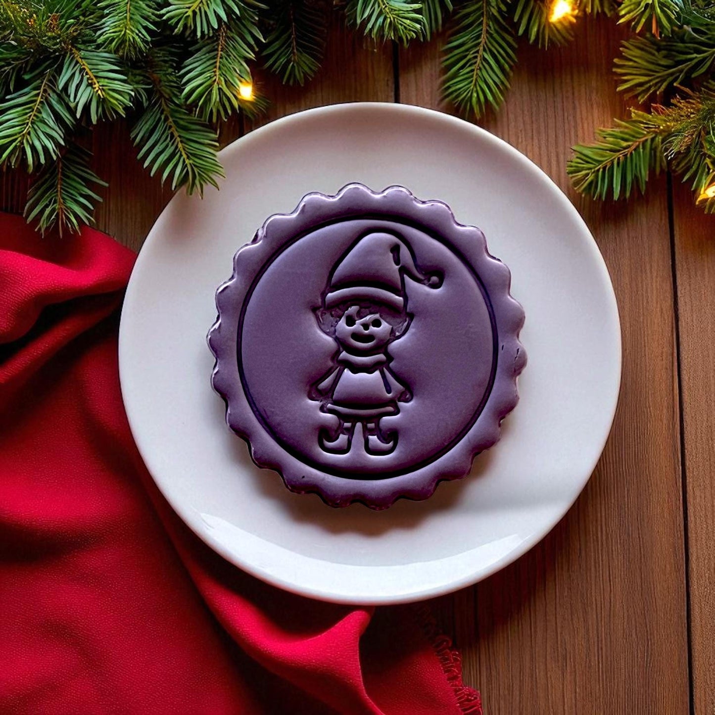 Purple elf clay imprint on clay slab with red fabric and holiday lights.