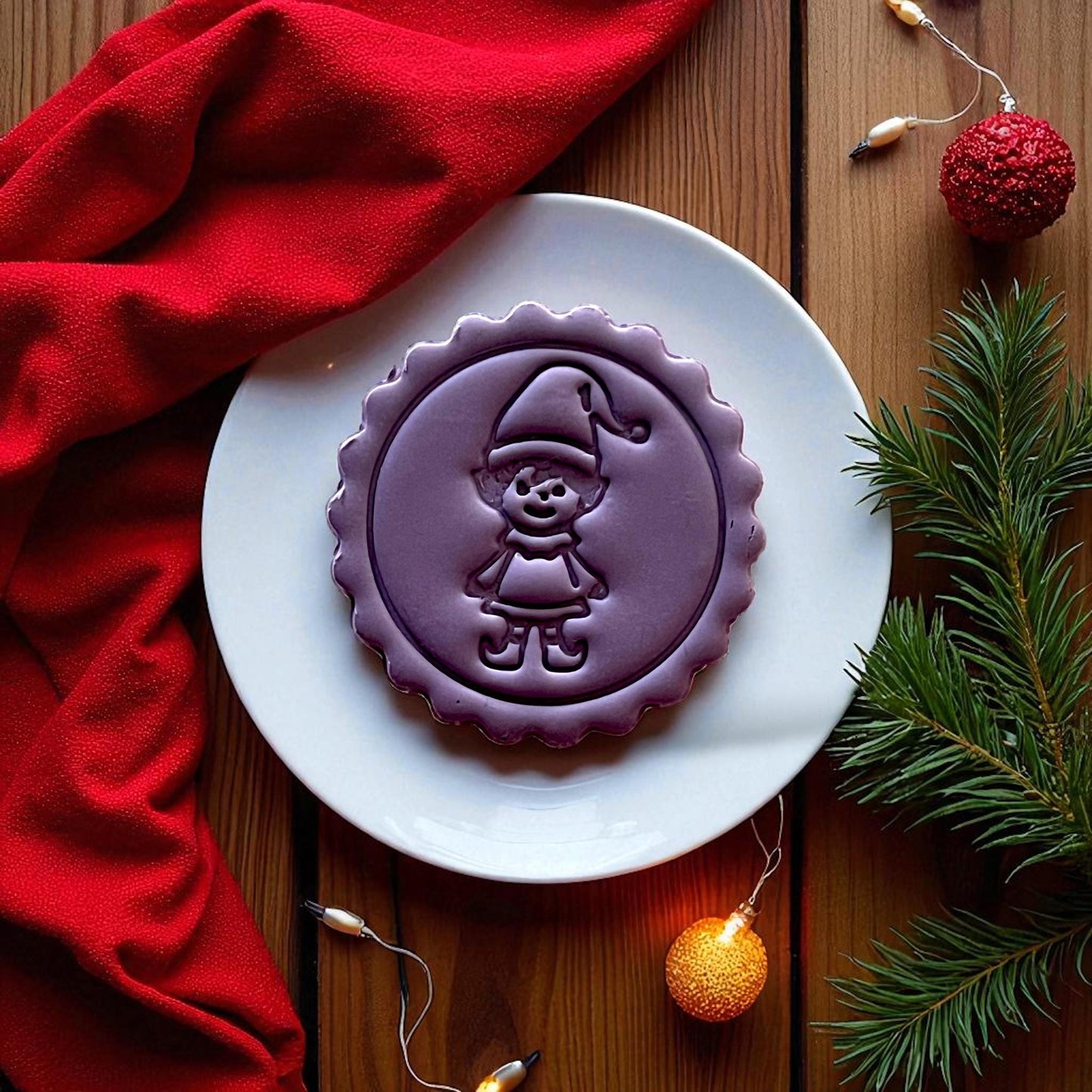 Purple elf clay imprint on clay slab with red fabric and holiday lights.