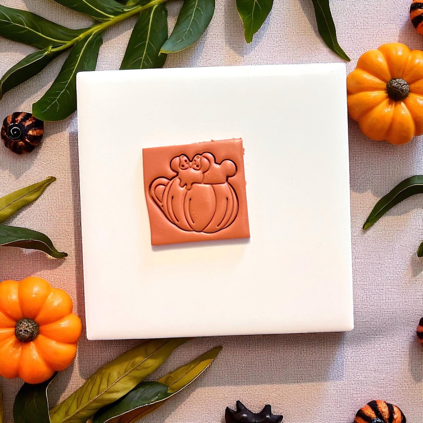 Close-up of pumpkin mug clay impression with ears and bow on a white tile