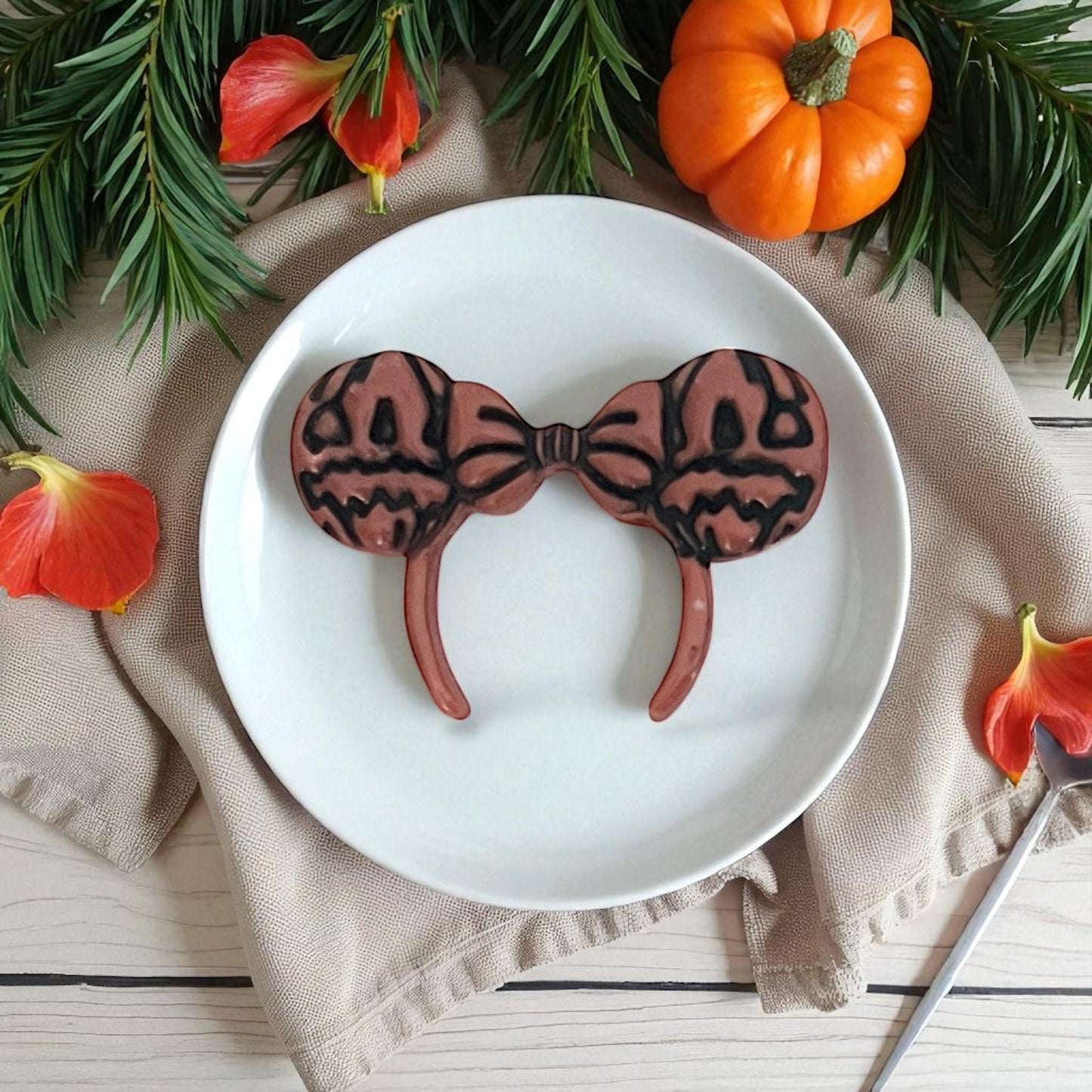 Brown pumpkin ears clay imprint with bow on white plate, greenery, and pumpkins.