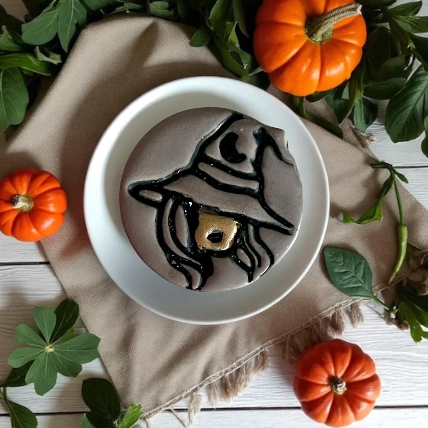 Large sexy witch clay piece on round plate surrounded by pumpkins and green leaves