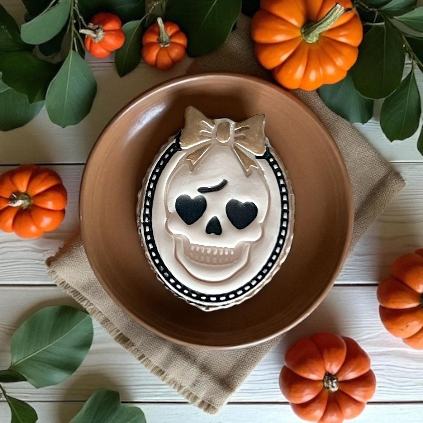 Decorated cookie shaped like girly skull cameo with bow in brown dish