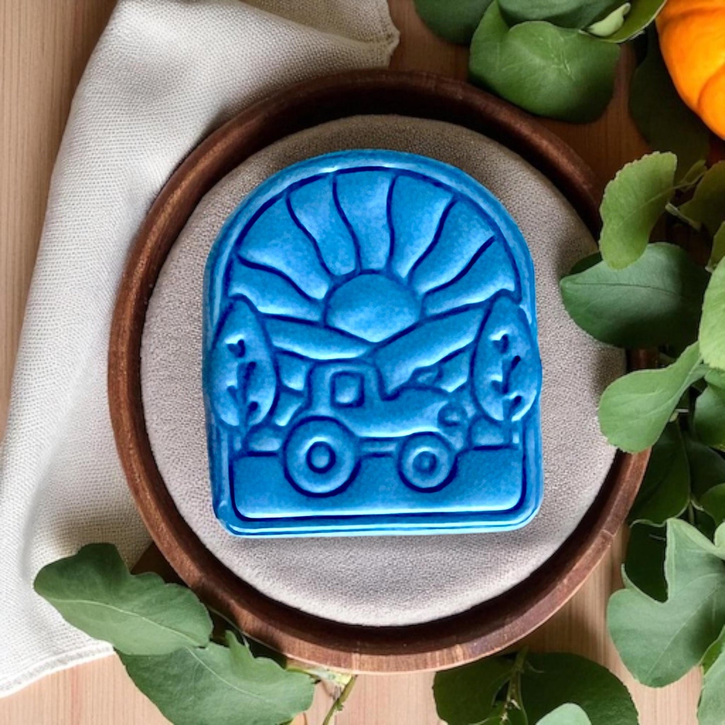 Blue clay impression of tractor under sunset with green leaves