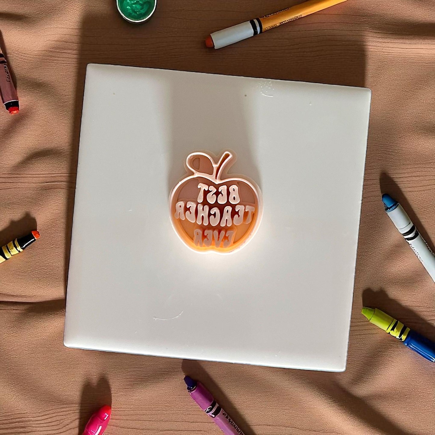 best teacher ever apple shaped polymer clay cutter on white tile surrounded by crayons
