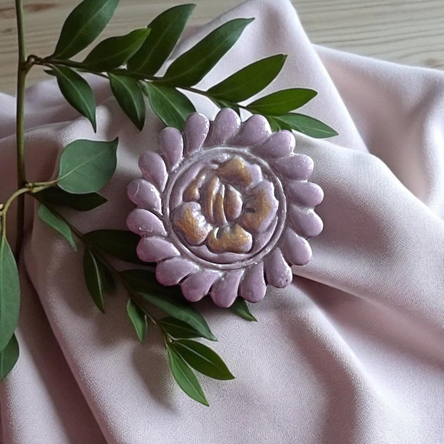 Large purple round flower clay piece with gold painted accents on fabric and greenery.