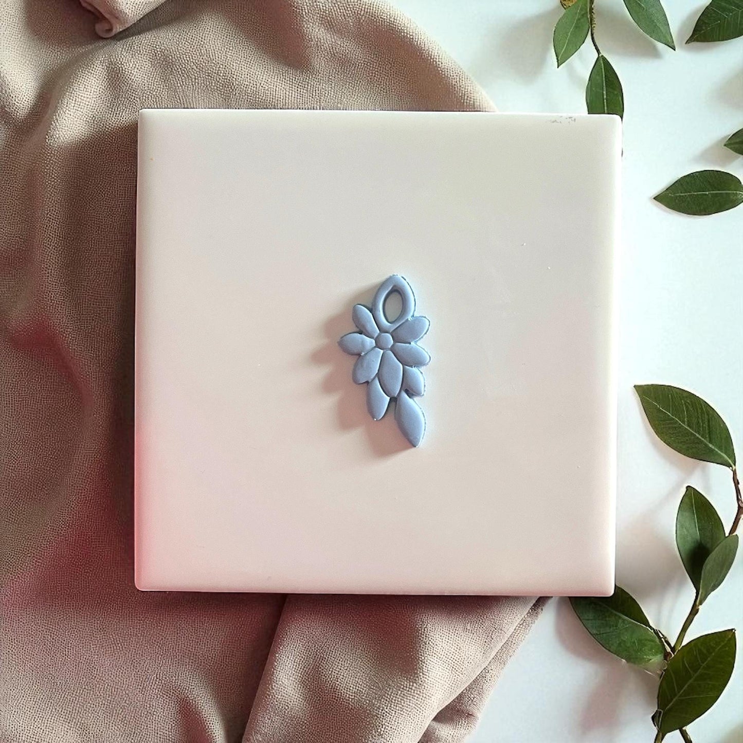 Blue floral clay imprint centered on white tile with leaves and fabric.