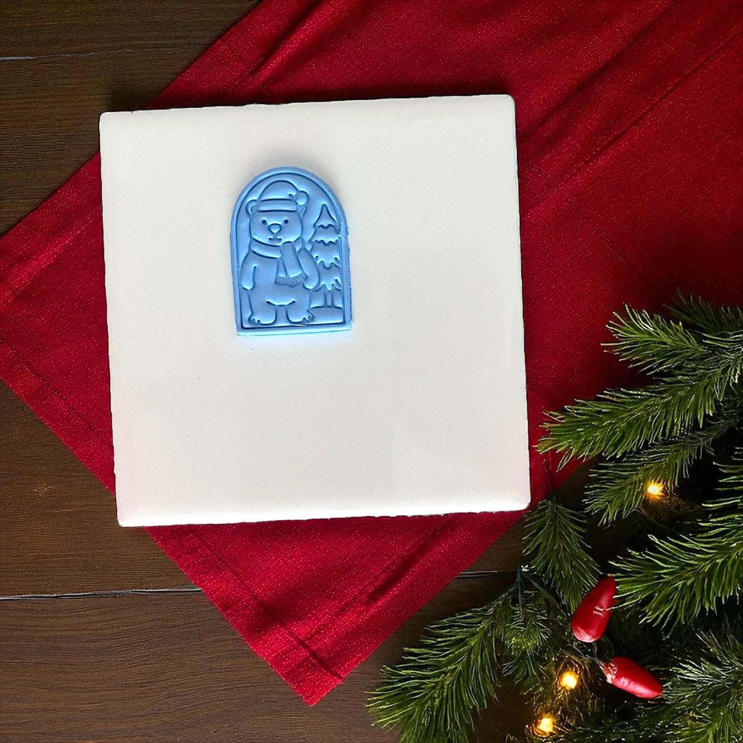 Blue polar bear clay imprint on white tile with red fabric and Christmas greenery.