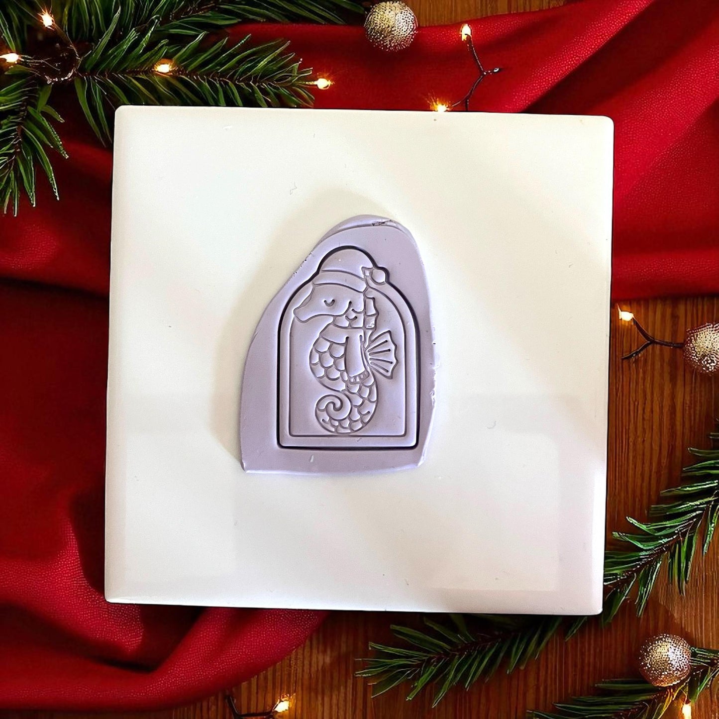 Purple seahorse clay imprint pressed into clay on white tile with holiday greenery.