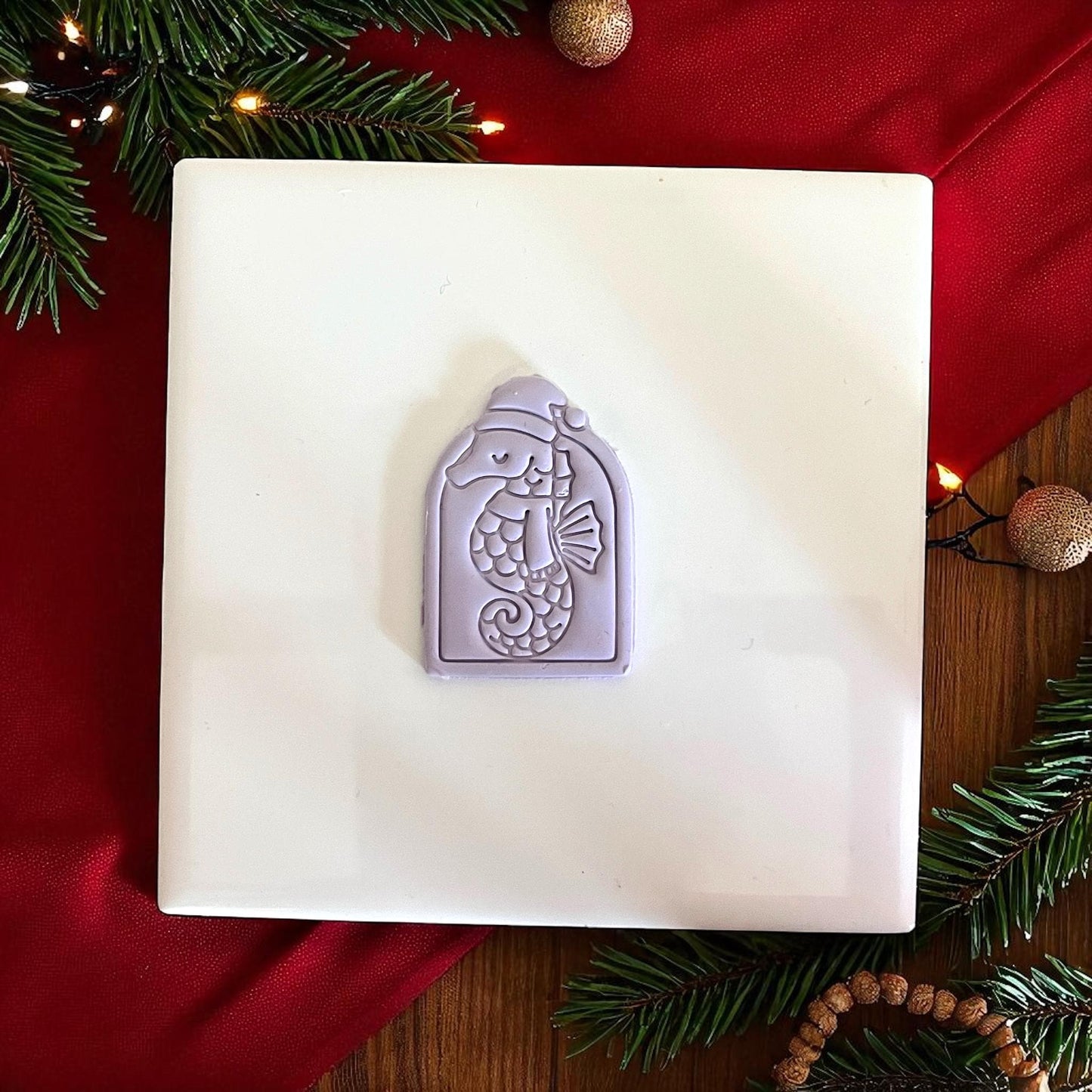 Purple seahorse clay imprint on white tile with red fabric and Christmas decorations.