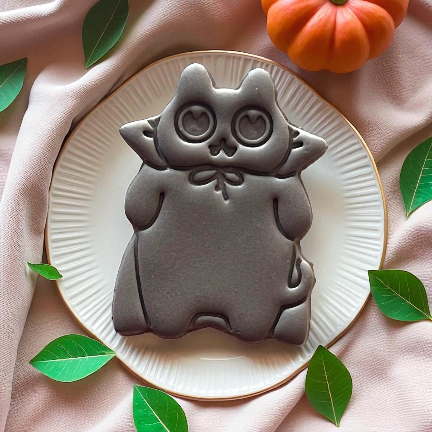 Large grey cat clay imprint with heart eyes on a white plate surrounded by leaves.