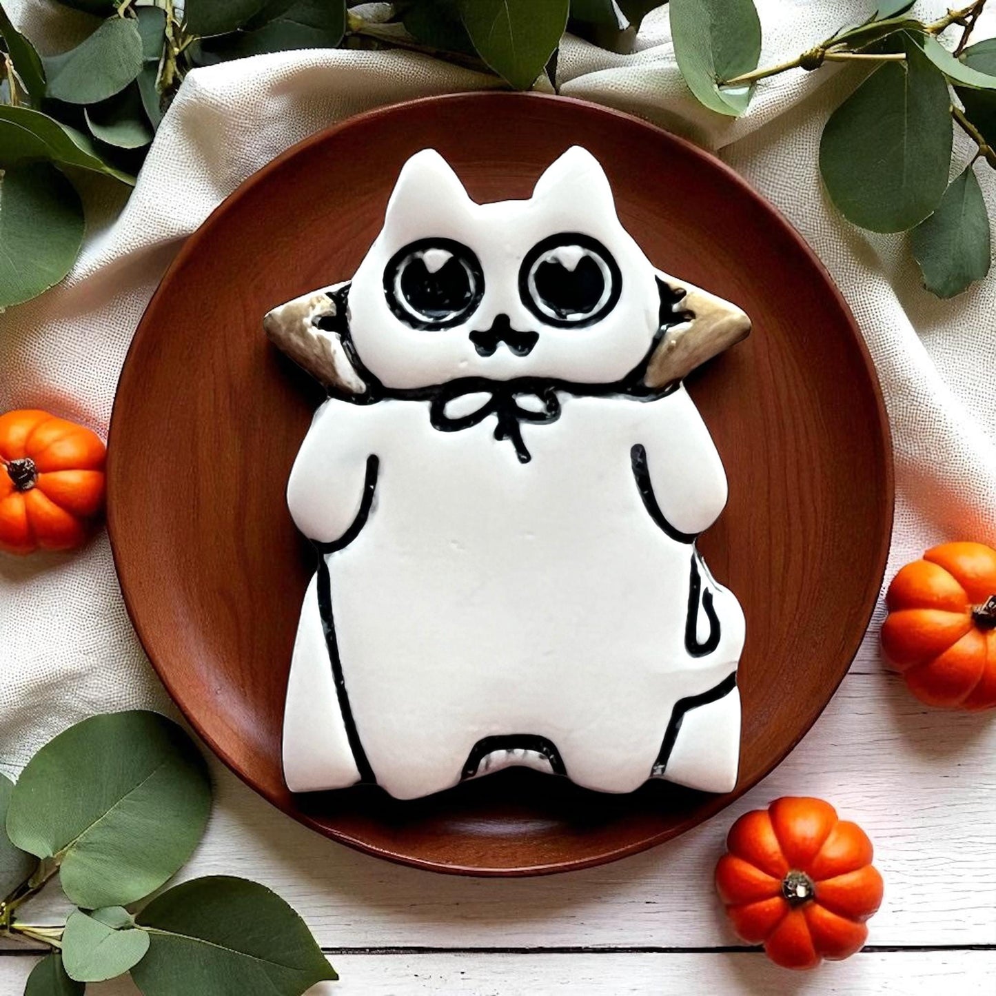 White decorated Halloween cat cookie with heart eyes on a brown plate with pumpkins.
