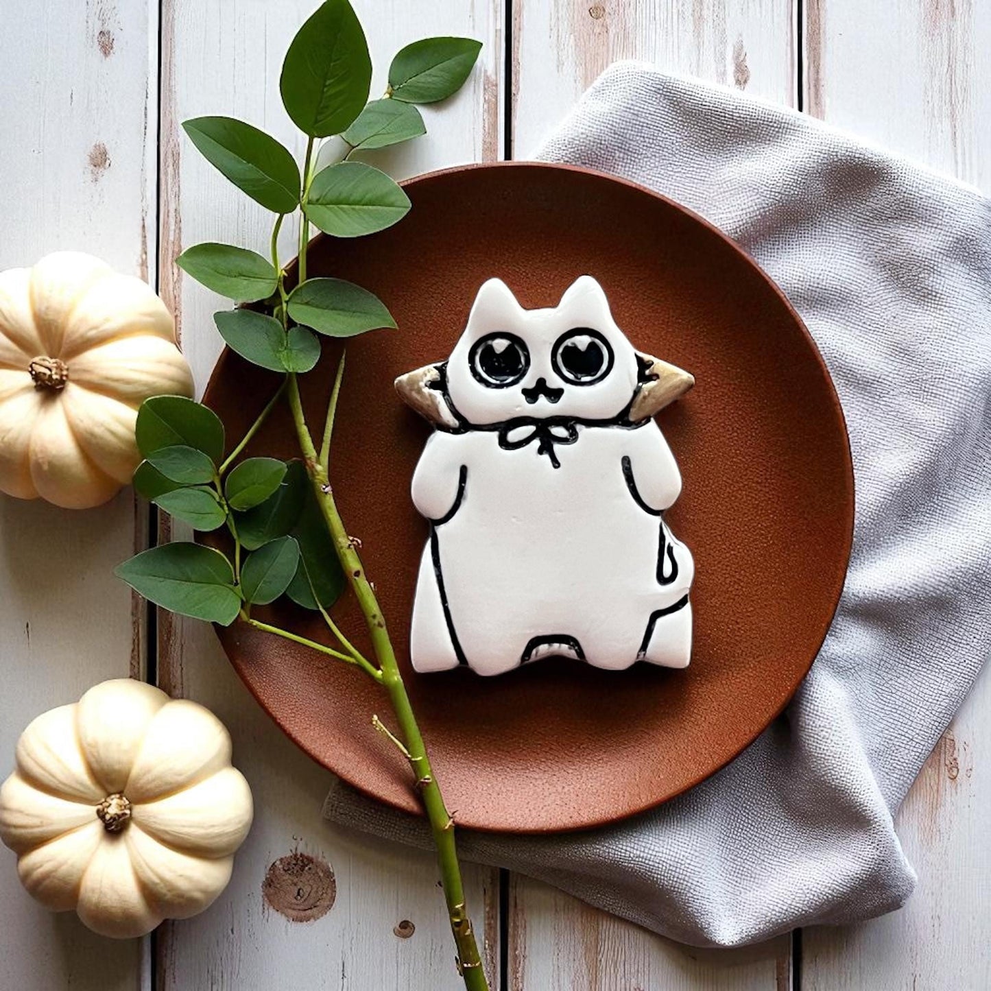 White decorated Halloween cat cookie with heart eyes on a brown plate with pumpkins.