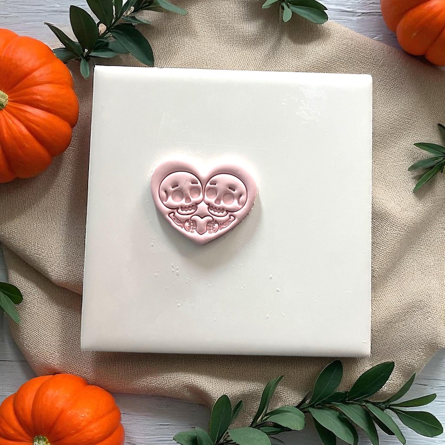 Pink clay skeleton couple heart design on white tile with pumpkins