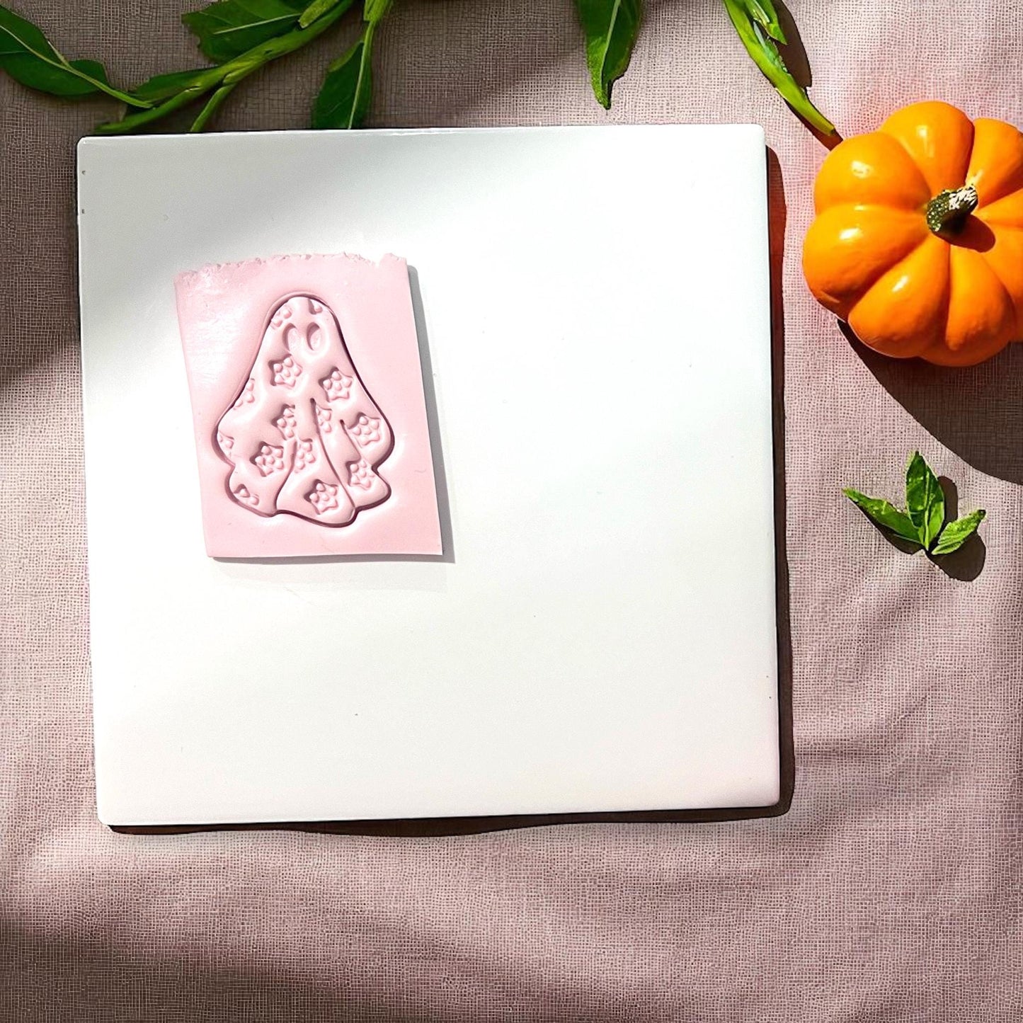 Pink floral ghost clay impression on white tile with pumpkins