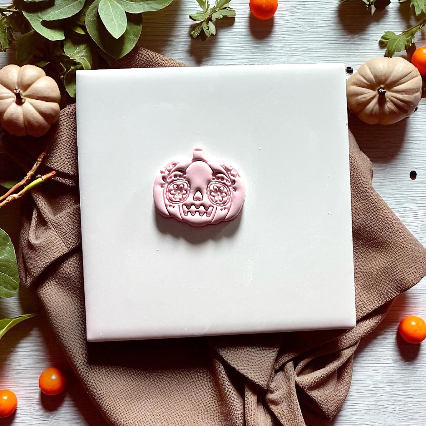 Sugar skull pumpkin clay imprint on white tile with greenery and pumpkins