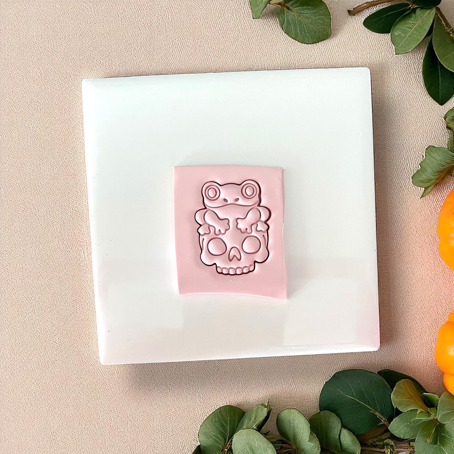 Pink frog on skull clay impression on white tile