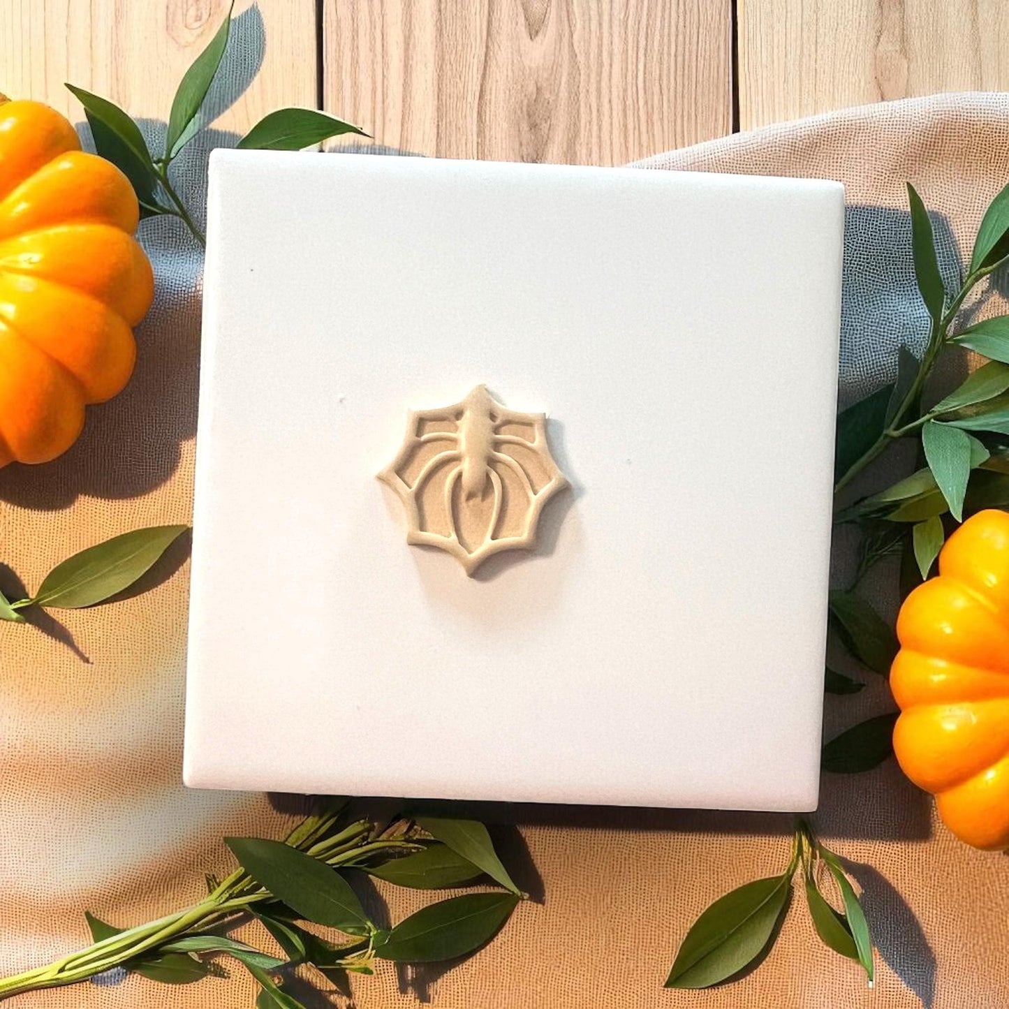 Small spider web clay imprint on white tile with pumpkins