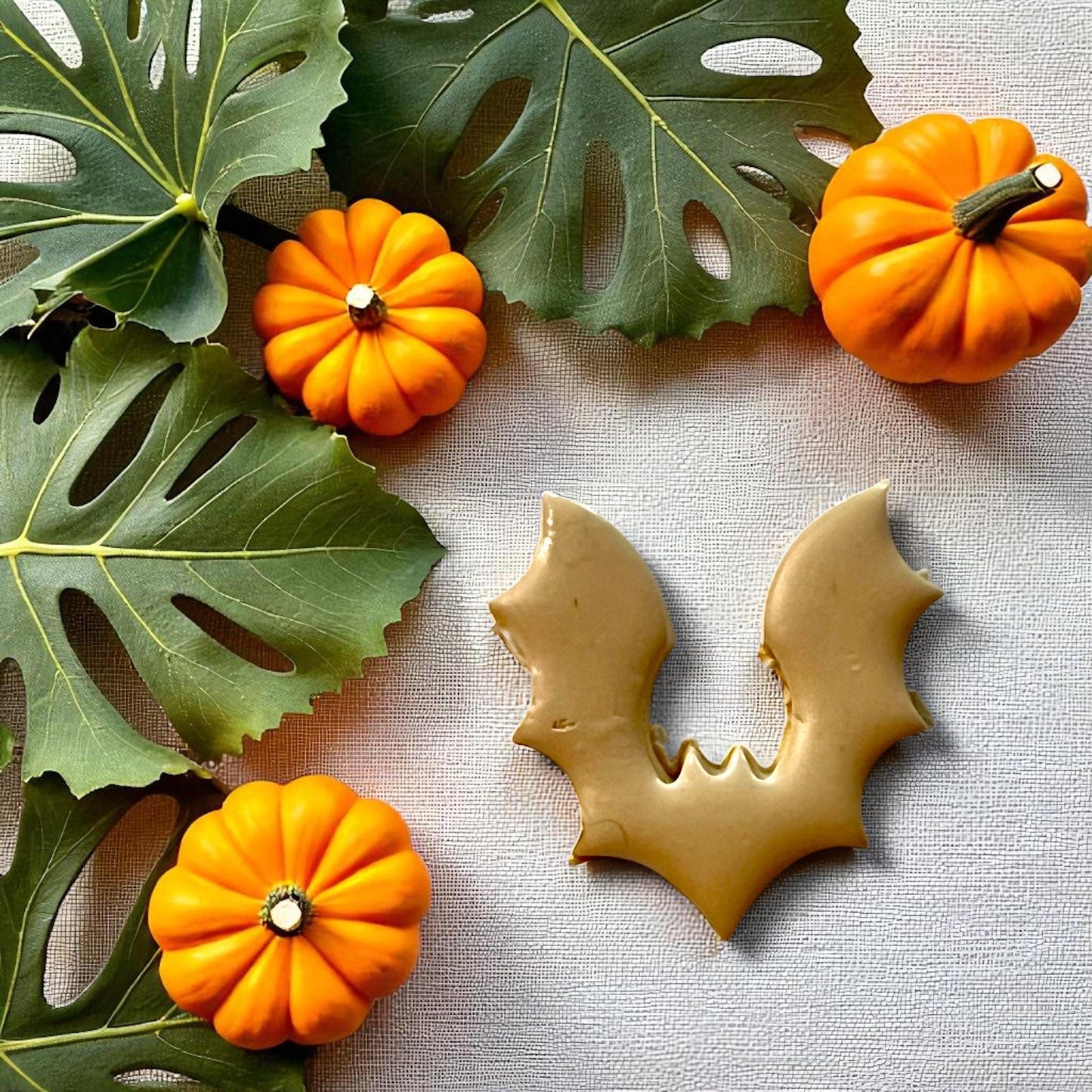 Bat clay imprint with pumpkins and tropical leaves on fabric background