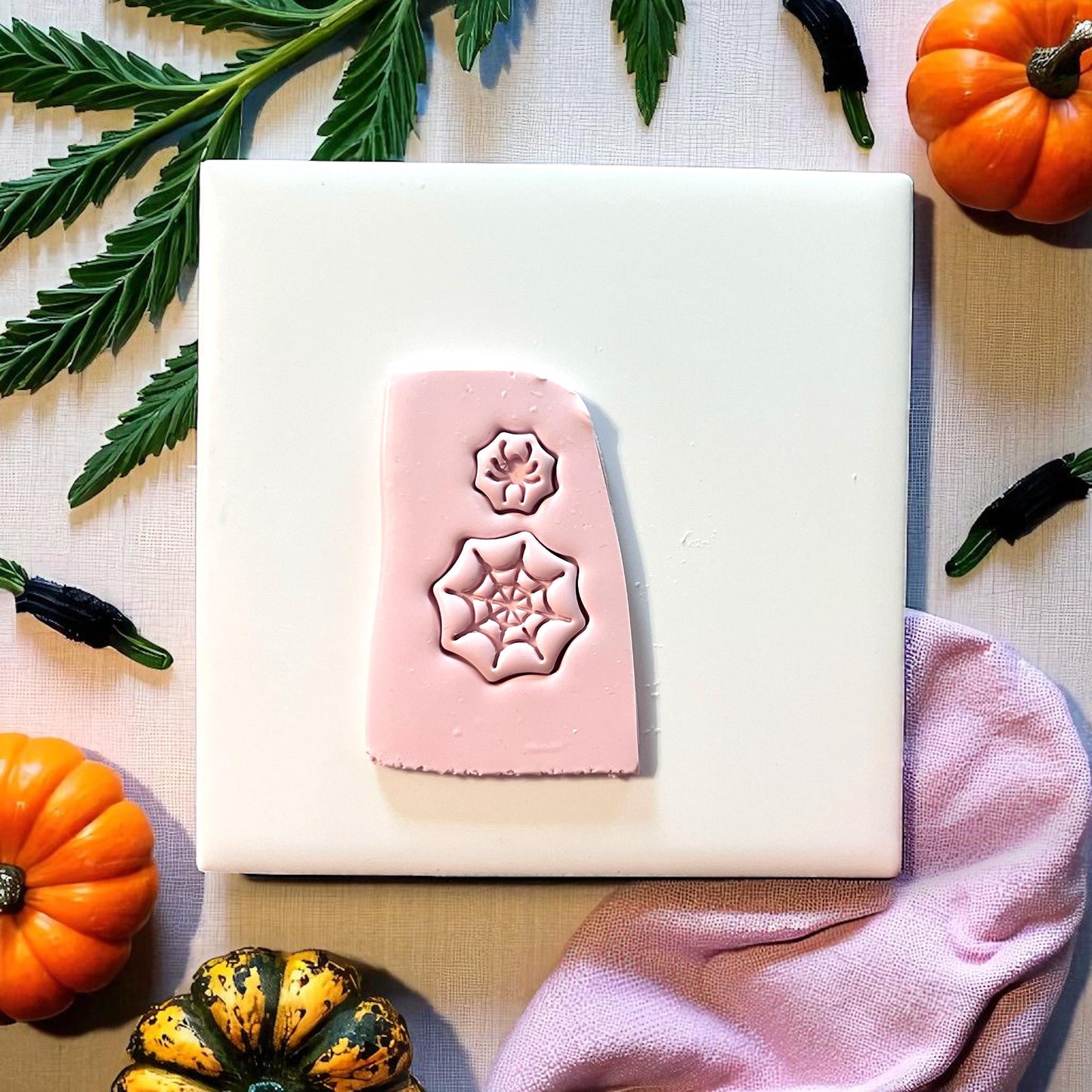 Pink clay slab with spiderweb and spider impressions surrounded by pumpkins